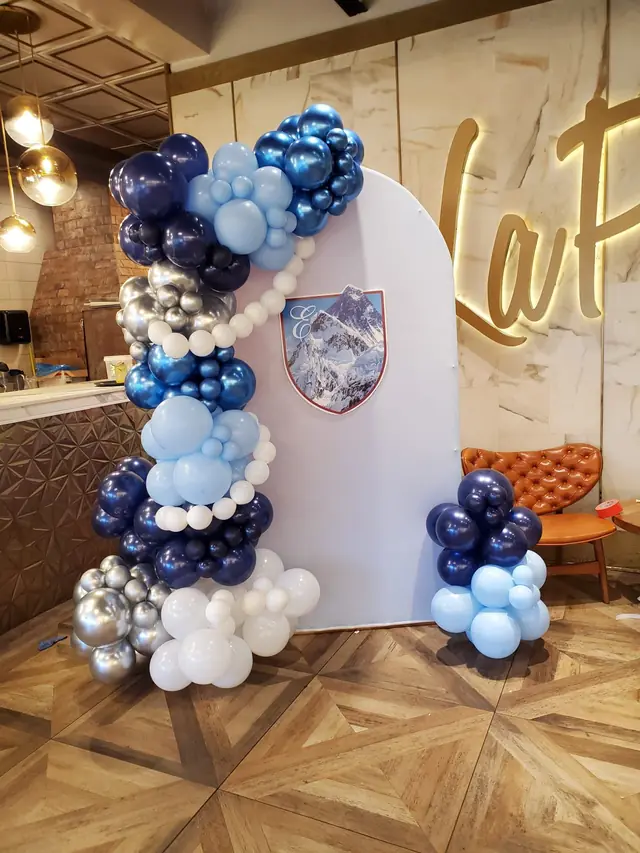 White arch backdrop with a navy, light blue and chrome silver balloon garland and a mountain crest