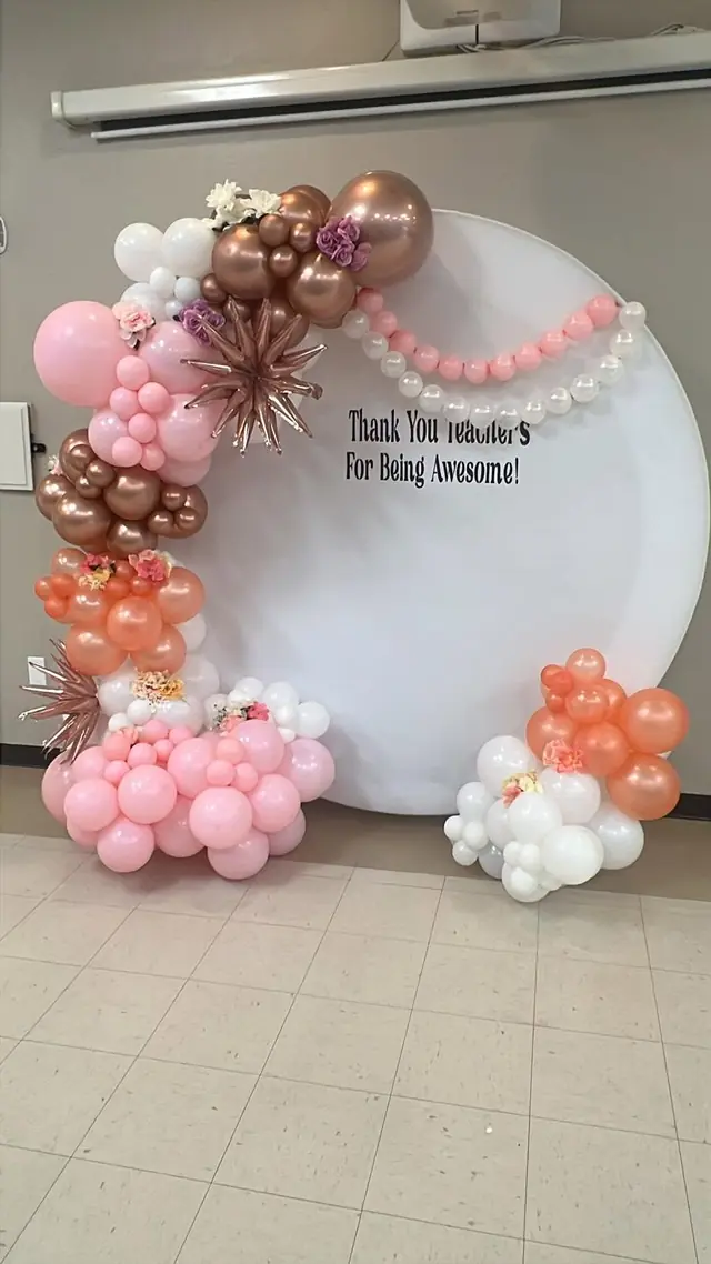 Round white backdrop reading Thank You Teachers with a pink, rose gold and coral balloon garland